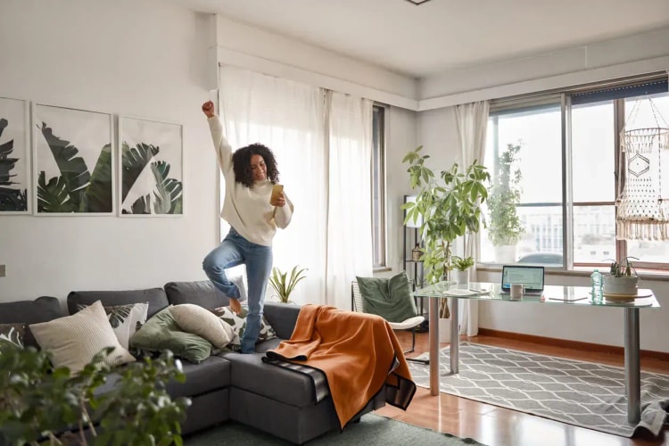 Jeune femme joyeuse dans son salon célébrant l’obtention d’un crédit immobilier